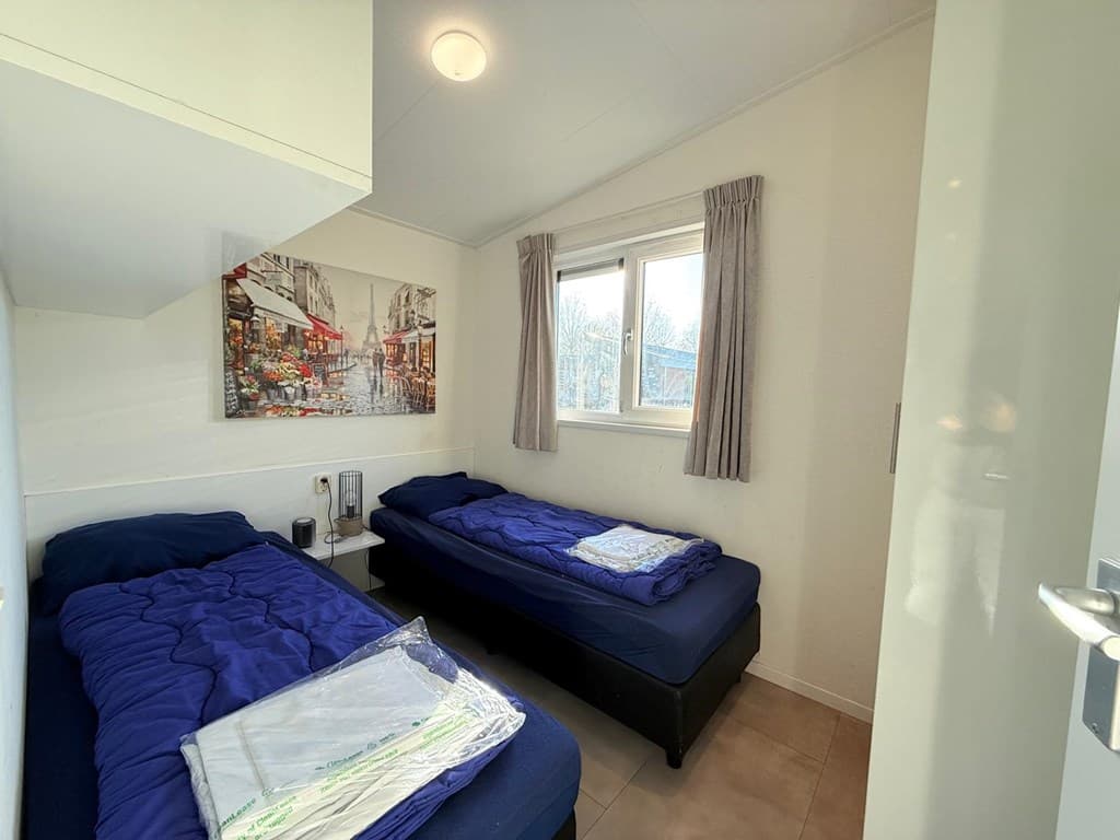 Slaapkamer met twee eenpersoonsbedden, raam met uitzicht en schilderij aan de wand.