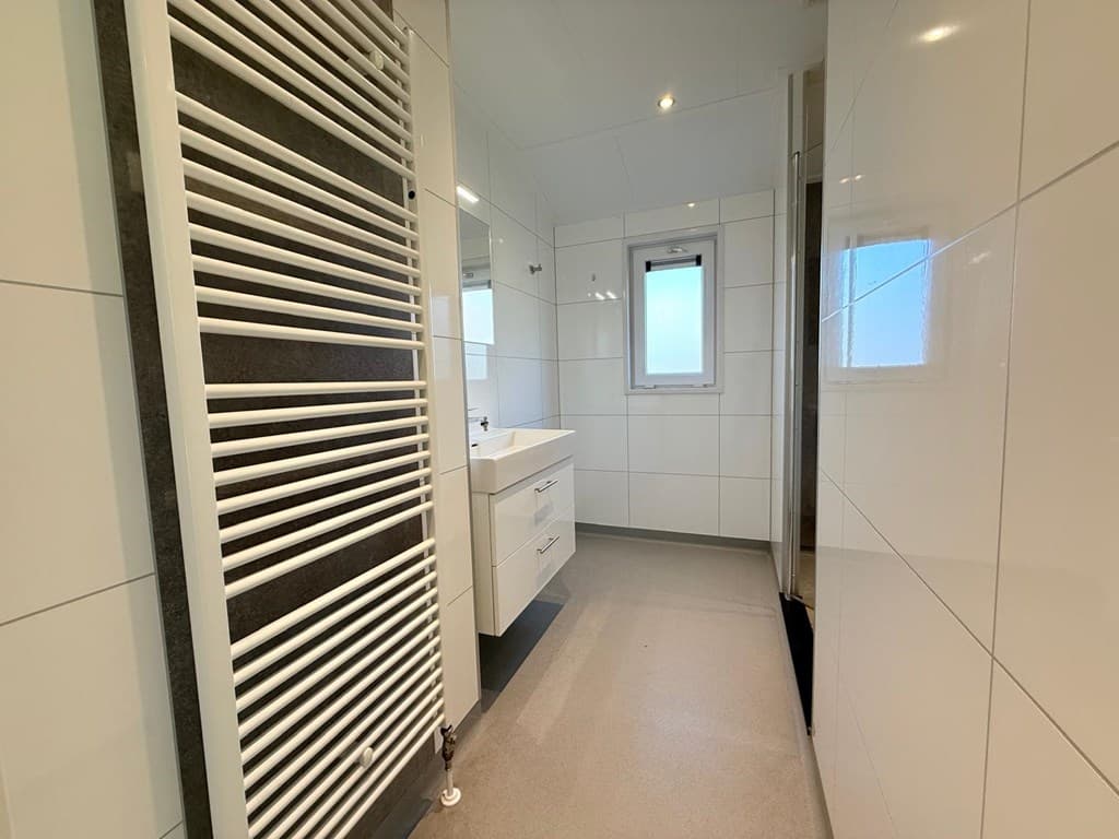 Moderne badkamer met witte tegels, een wastafel met lades en een handdoekenradiator tegen de muur.