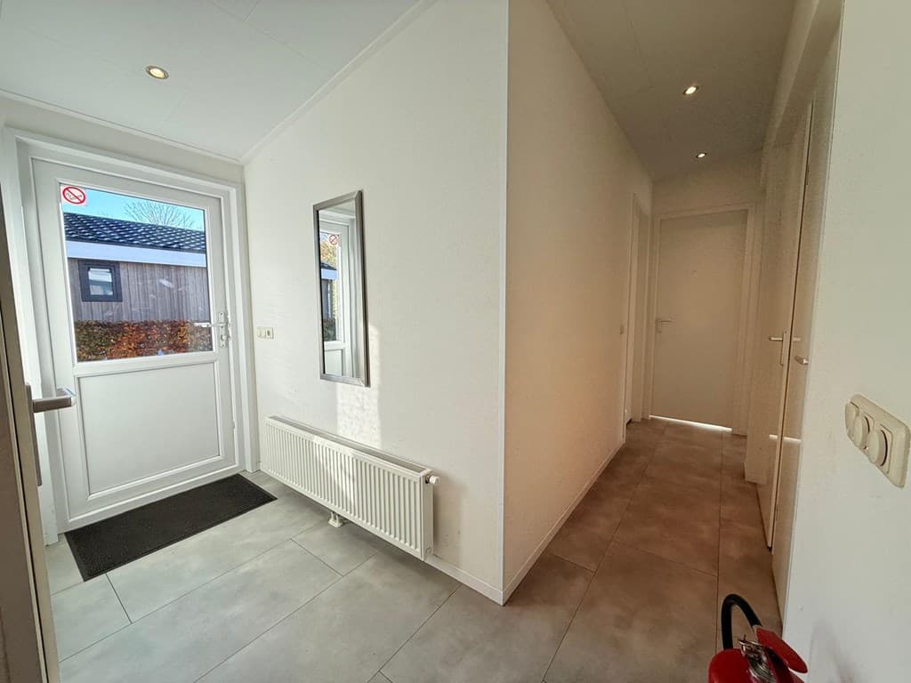 Ingang van een woning met een lichte hal, een spiegel, een radiator en een deur naar een andere ruimte.