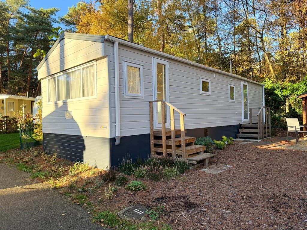 Buitenzicht van een lichte vakantiewoning met houten trappen en omgeven door bomen en groen.