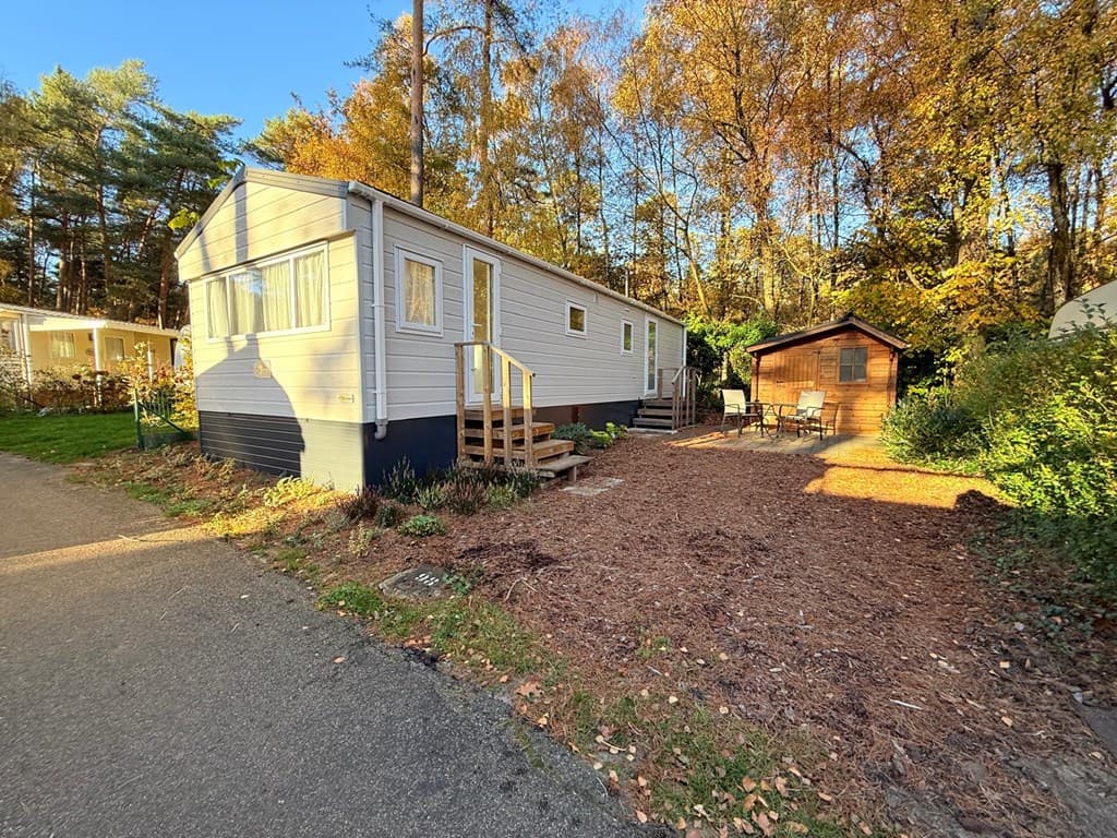 Mobiel huis met houten veranda en tuin, omgeven door bomen op Camping Zavelbos in Maaseik.
