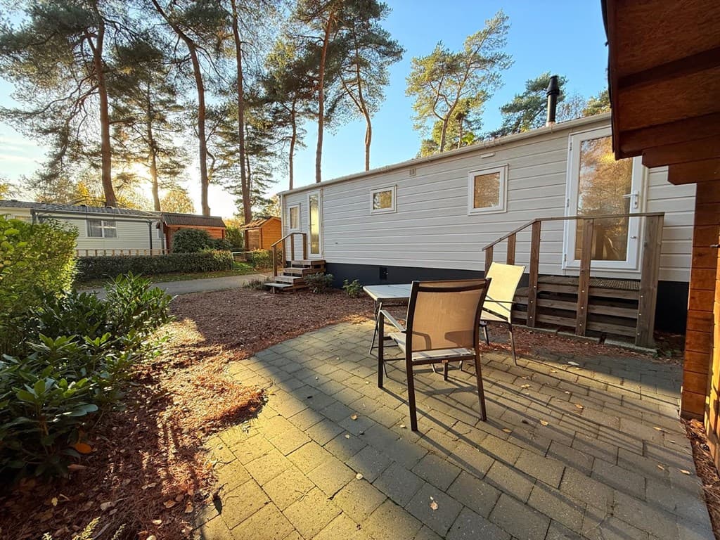 Terras met zitmeubelen, omgeven door groen, met een mobiele woning en bomen op de achtergrond