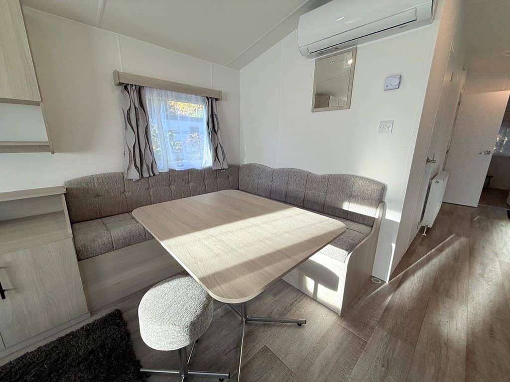 Interieur van een vakantiewoning met een zithoek en een tafel bij een raam, lichte wanden en vloeren van laminaat.