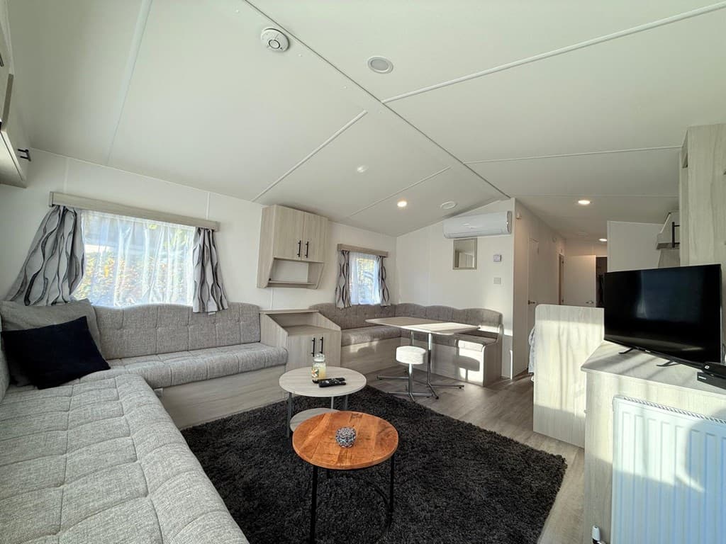 Moderne woonkamer met zithoek, eettafel en kitchenette in lichte tinten, grote ramen zorgen voor natuurlijk licht