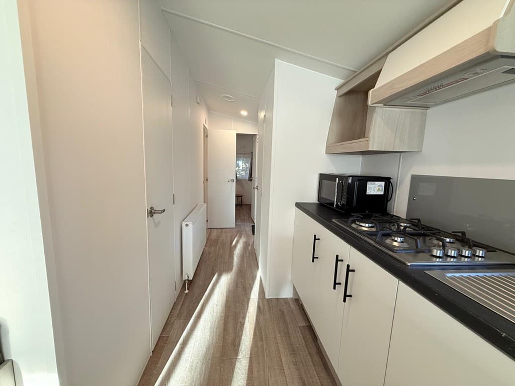 Keukenruimte met zicht op gang, voorzien van gasfornuis, afzuigkap en magnetron, strakke moderne inrichting en veel lichtinva