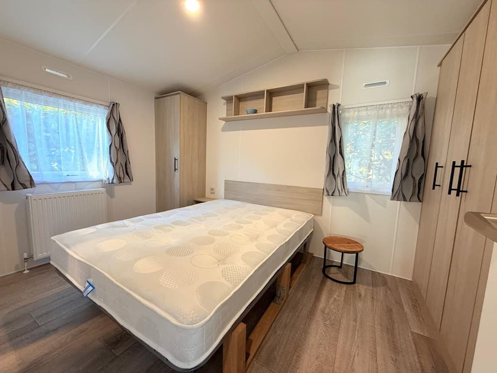 Slaapkamer met tweepersoonsbed, houten kast en lichte raambekleding in een bungalow op Camping Zavelbos.