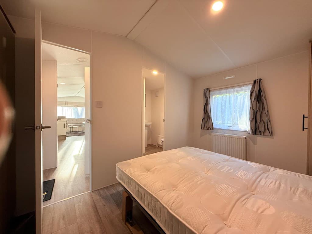 Slaapkamer met een bed en zicht op een deur naar een andere ruimte, lichte wanden en raam met gordijnen