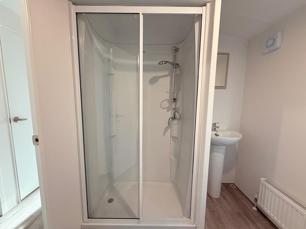 Douchecabine met glazen deuren en een wastafel in een eenvoudige badkamer