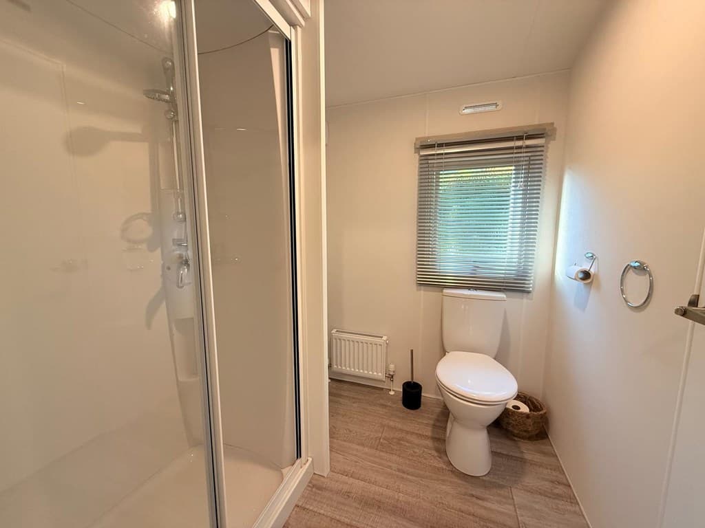 Moderne badkamer met douche, toilet en een raam met zonwering.