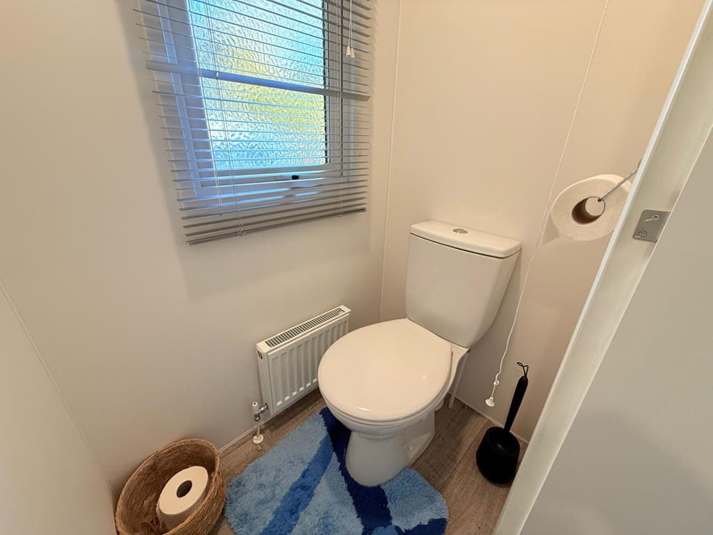 Badkamer met toilet, raam met jaloezieën, vloerkleed en handdoekenhouder aan de wand.
