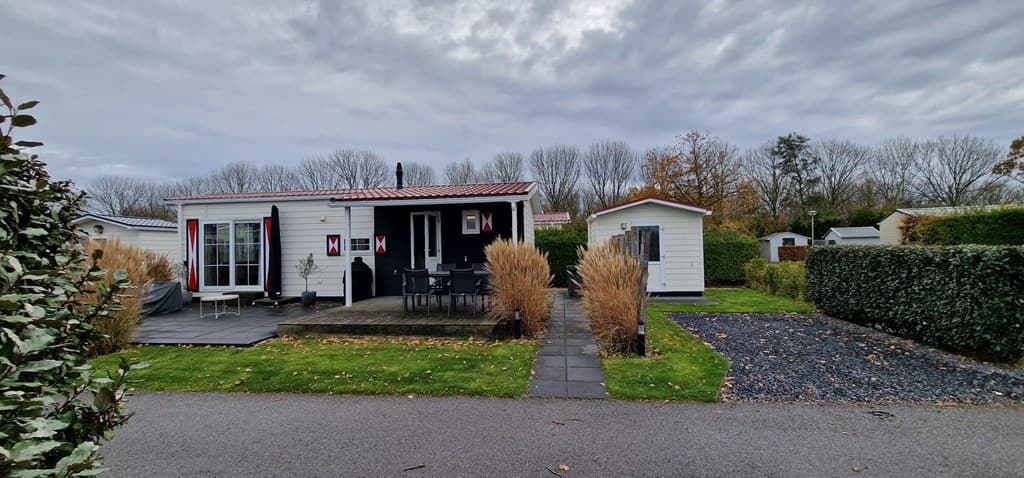 Vakantiehuis met veranda, grijze tegels en houtendecoratie, omgeven door groen en grindpaden.