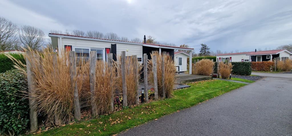 Moderne vakantiewoning met een terrassentrap en omringd door hoge siergrassen, gelegen langs een groene laan