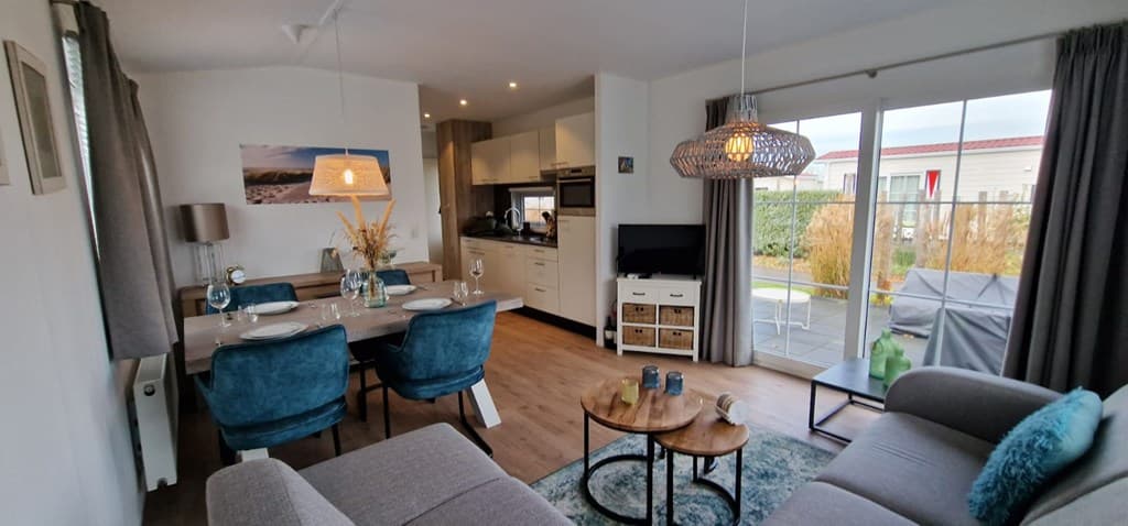 Woonkamer met eetgedeelte, moderne inrichting en toegang tot een terras met tuinzicht.