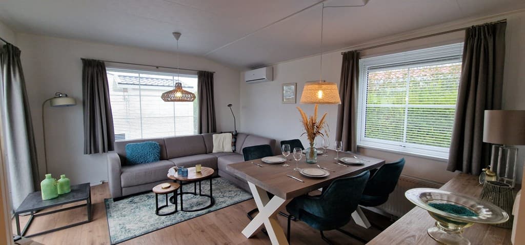 Woonkamer met een zithoek, eettafel en moderne decoraties, veel natuurlijk licht door de ramen.