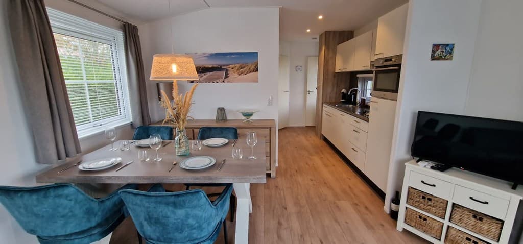 Eetruimte met een houten tafel en stoelen, moderne keuken en natuurlijke lichtinval door het raam