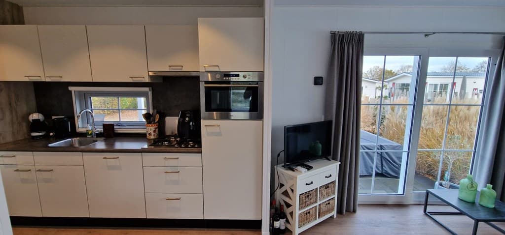 Moderne keuken met inbouwapparatuur en een zithoek met televisie en grote ramen naar buiten.