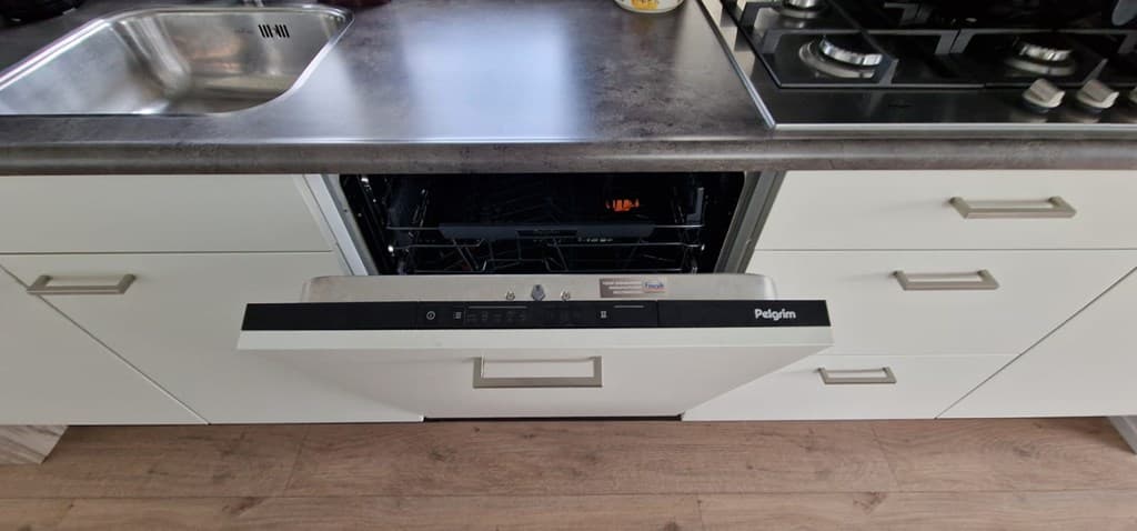 Keuken met een moderne afwasmachine, spoelbak en kookplaat op een donker werkblad met lichte kasten eromheen