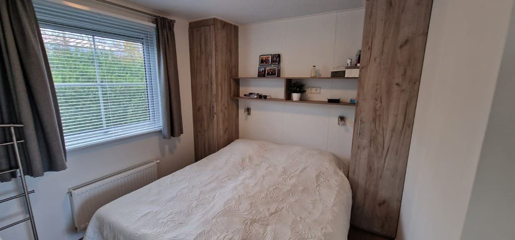 Slaapkamer met een tweepersoonsbed, een raam met jaloezieën en wandplanken met decoraties.