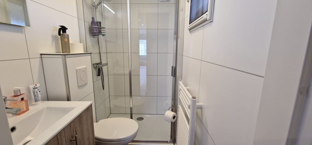 Moderne badkamer met inloopdouche, wastafel en toilet in lichte tinten.