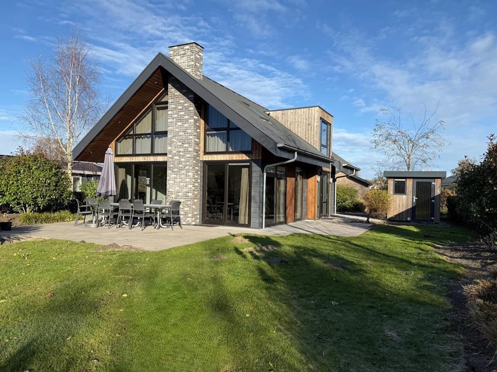 Moderne vakantiewoning met houten gevel, grote ramen en patio met tuinmeubilair in EuroParcs Zuiderzee