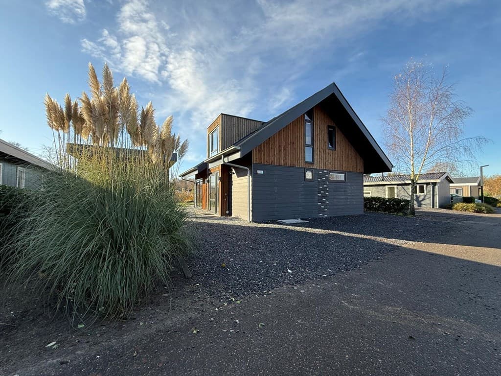 Moderne vakantiewoning met houten gevels en een schuin dak, omgeven door groen en grindpaden in EuroParcs Zuiderzee.