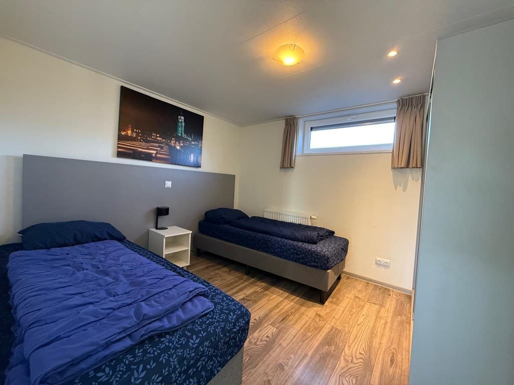 Slaapkamer met twee eenpersoonsbedden, nachtkastje en raam met zicht op buitenlucht.