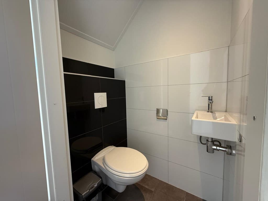Wc met wandtegels in zwart en wit, toilet en kleine wastafel zijn zichtbaar.