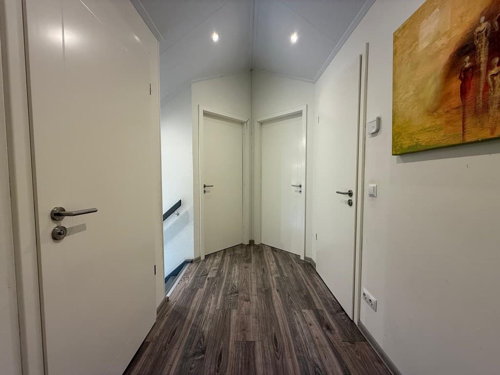 Lichte hal met meerdere deuren en een trap naar boven, laminaatvloer en modern wanddecoratie.