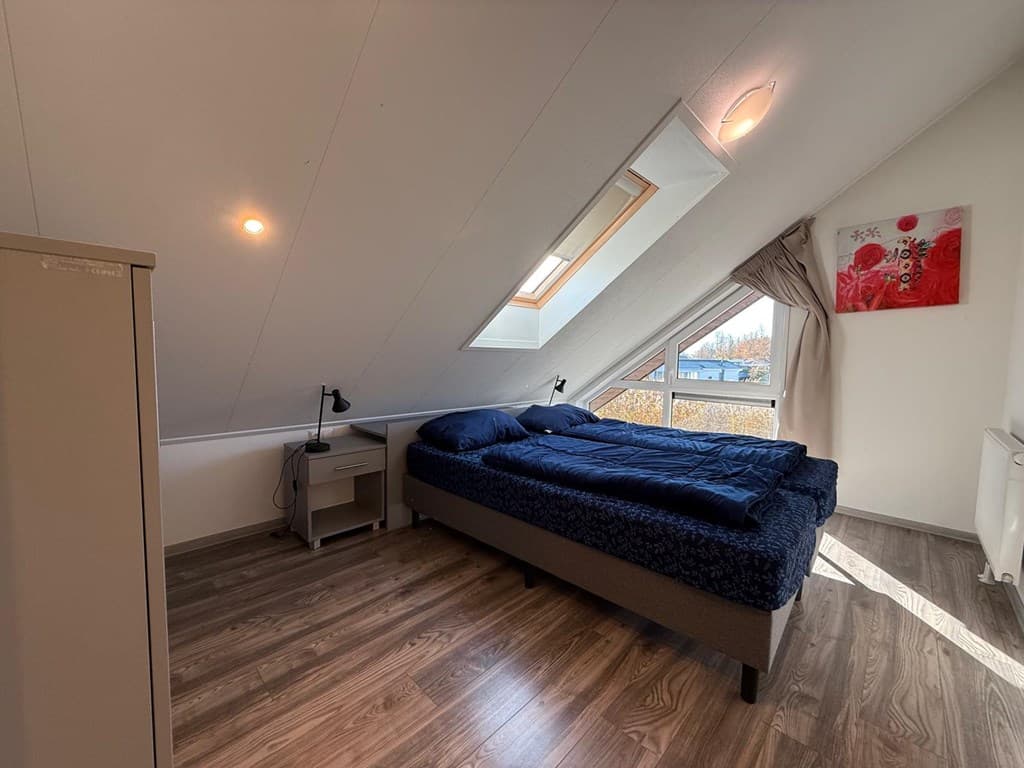 Sfeervolle slaapkamer onder het schuine dak met twee eenpersoonsbedden en natuurlijk licht door het raam