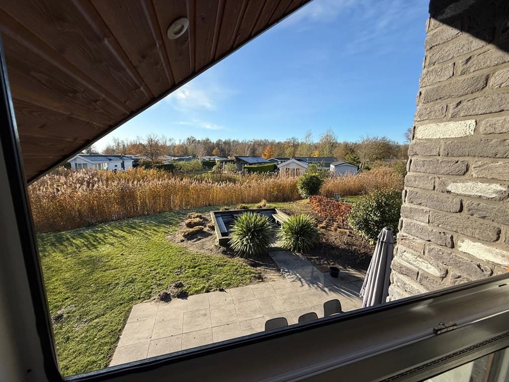 Uitzicht vanuit de woning over een tuin met gras, stenen terras en planten aan de rand van een vakantieresort.