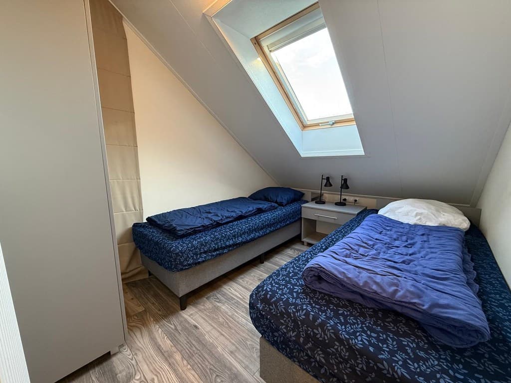 Sfeervolle slaapkamer met twee eenpersoonsbedden, nachtkastjes en een dakraam voor natuurlijk licht