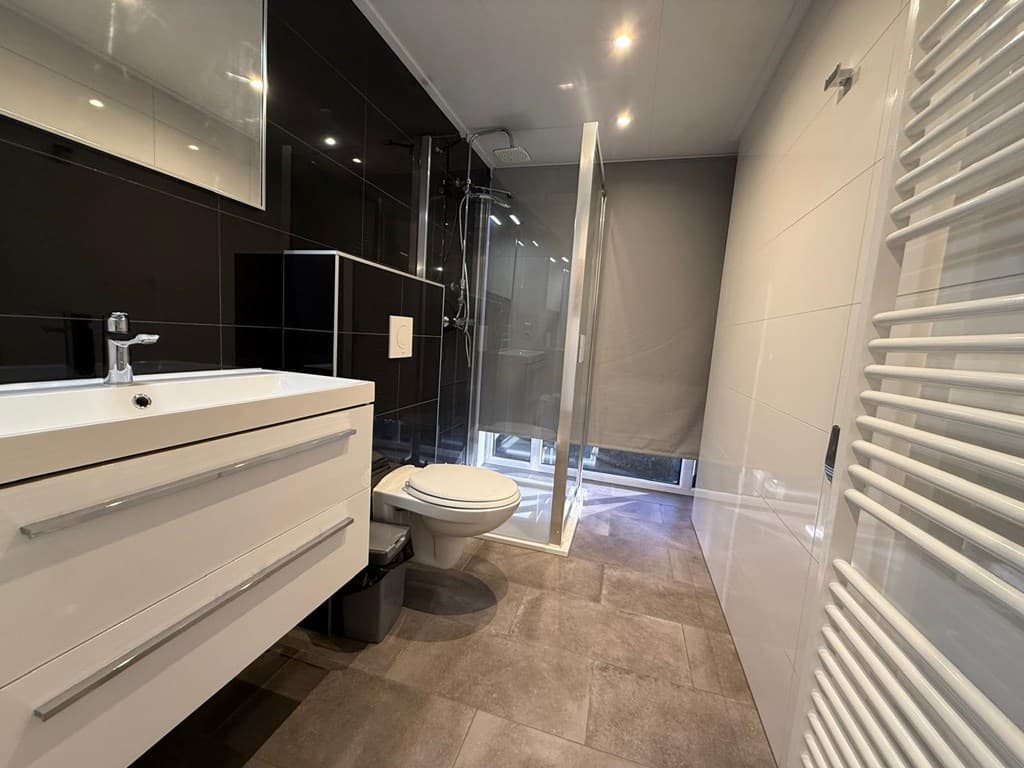 Moderne badkamer met douche, wastafel en toilet, betegeld in zwart en wit met vloerverwarming.
