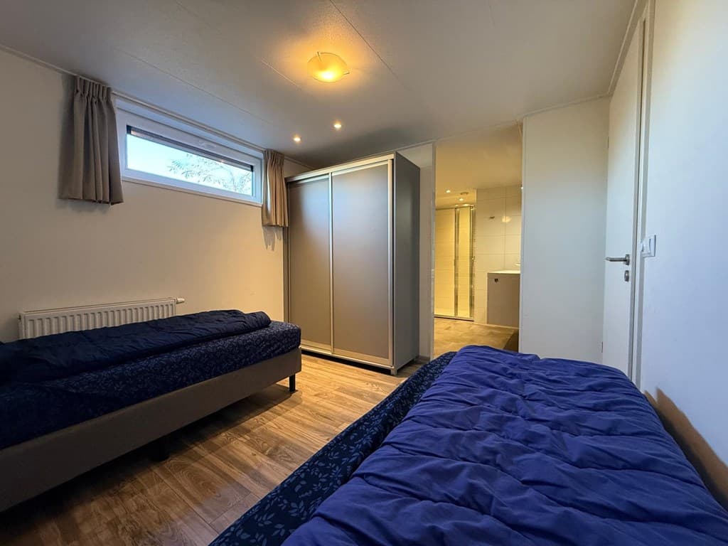 Slaapkamer met twee aparte bedden, kast en doorgang naar badkamer met moderne inrichting en licht tegelwerk