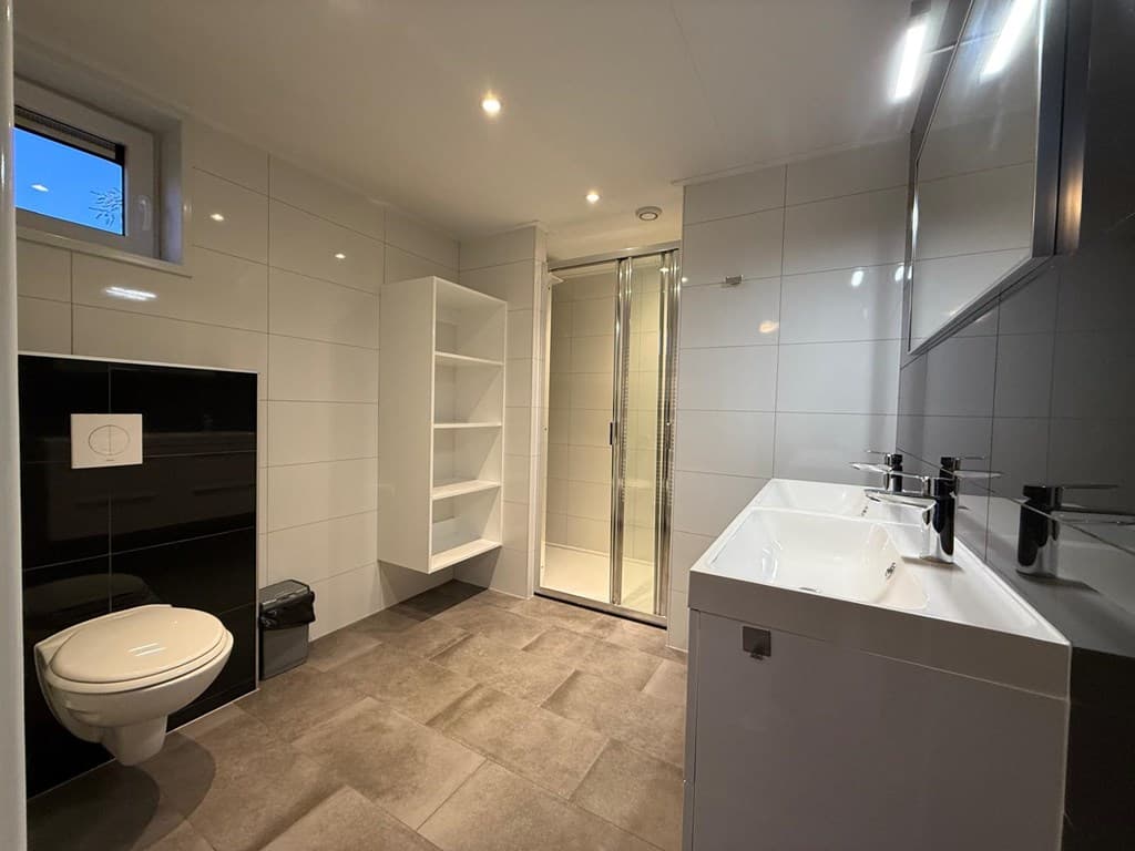 Moderne badkamer met wastafels, douchecabine, toilet en open schappen in een neutrale kleurstelling.