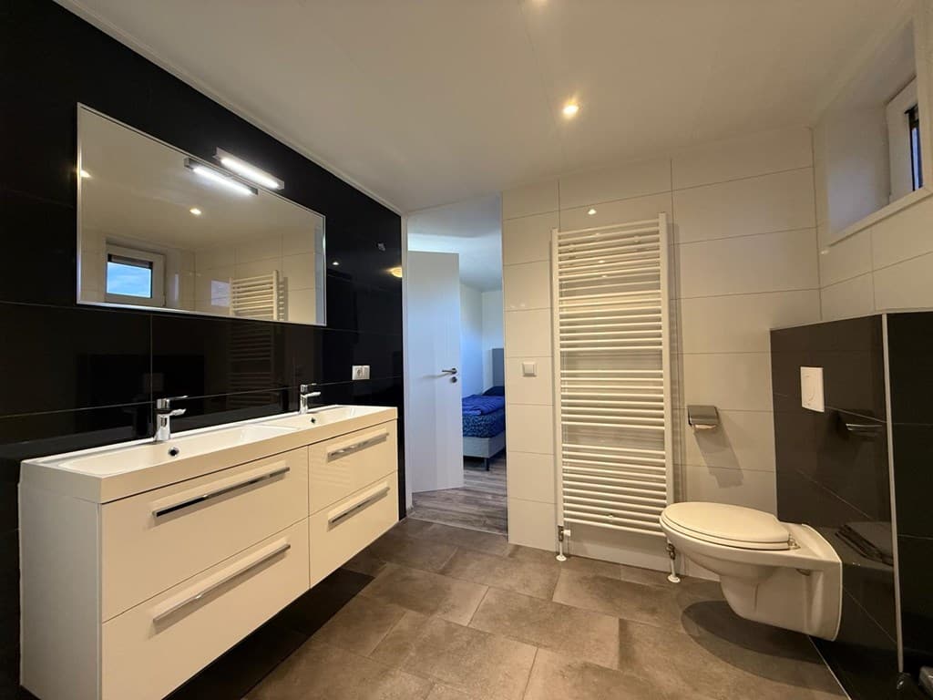 Strak badkamer met dubbele wastafel, toilet, radiator en modern tegelwerk in zwart en wit.