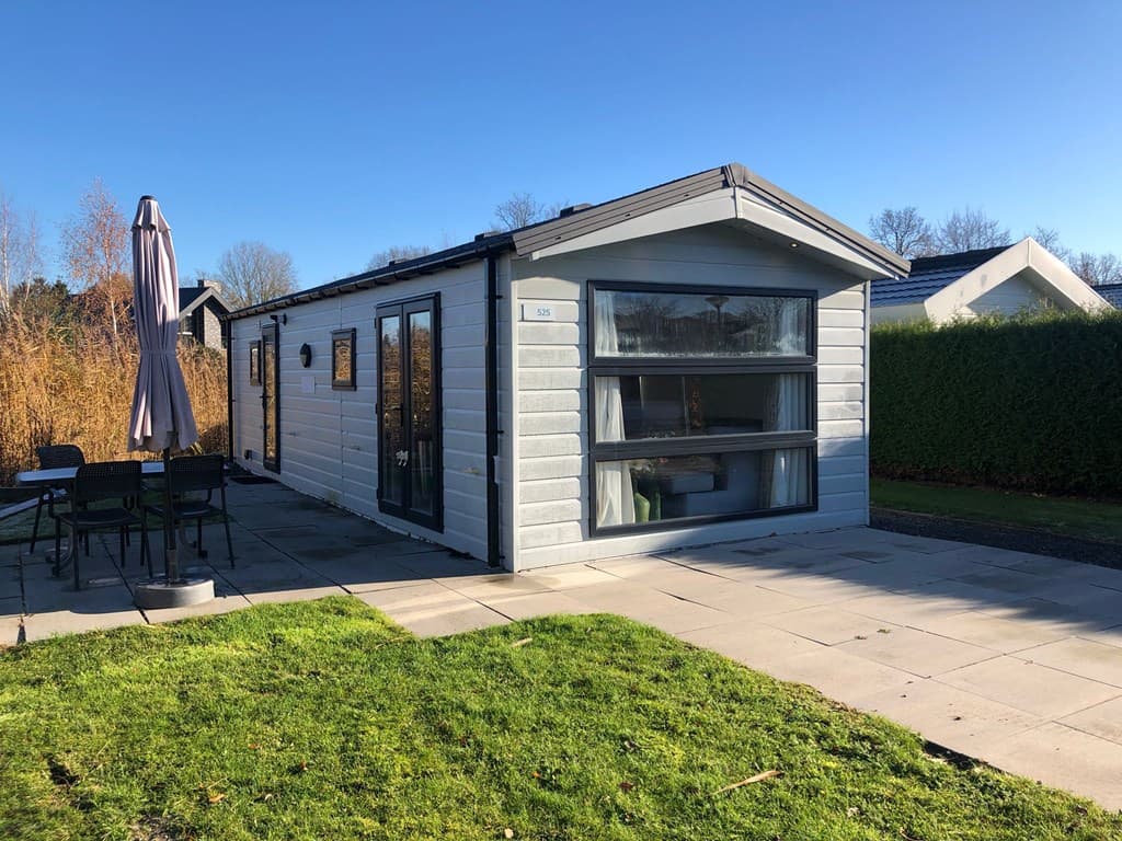 Vakantiewoning met lichtgrijze gevel, terras met parasol en tuinmeubilair, gelegen in een groene omgeving.