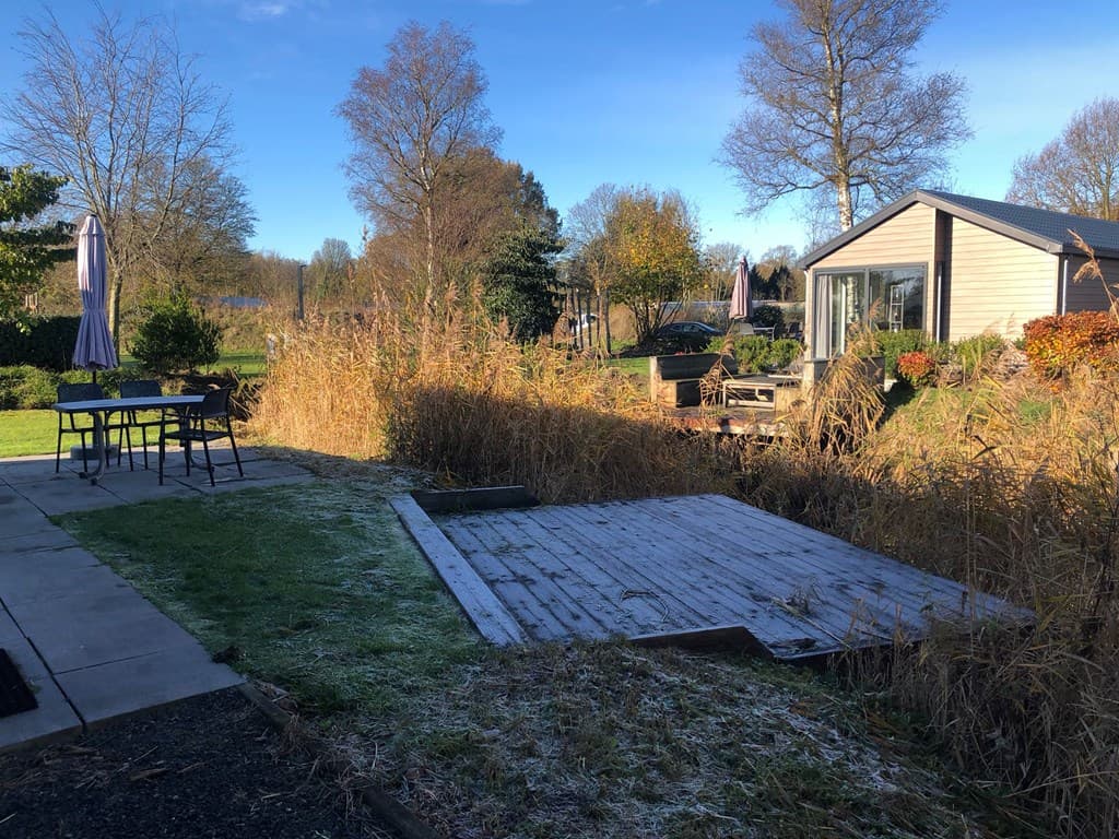 Buitenaanzicht van een woning met een houten terras, gras, tuinmeubilair en bomen in EuroParcs Zuiderzee.