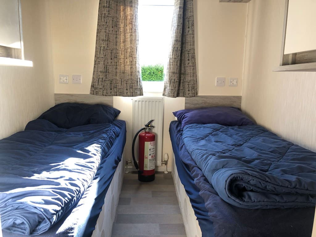 Slaapkamer met twee eenpersoonsbedden, een raam en een brandblusser tussen de bedden.
