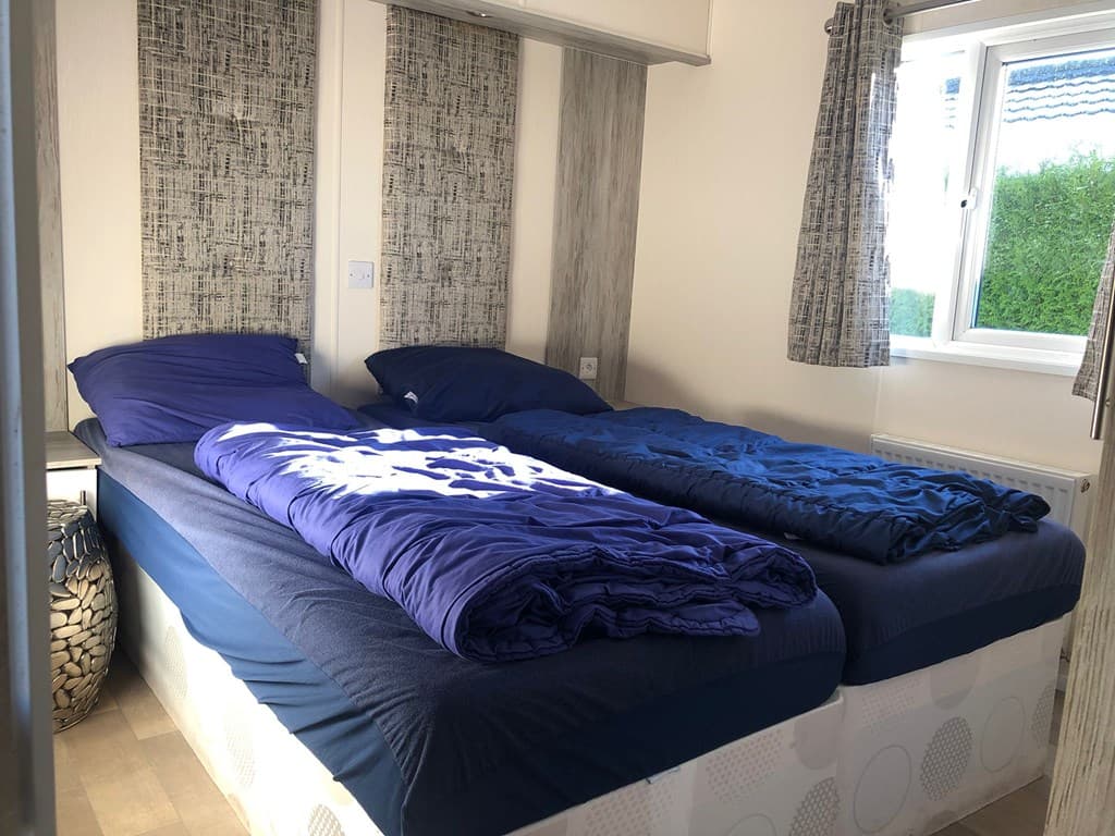 Slaapkamer met twee aparte bedden, blauw beddengoed en een raam met uitzicht op de buitenruimte.