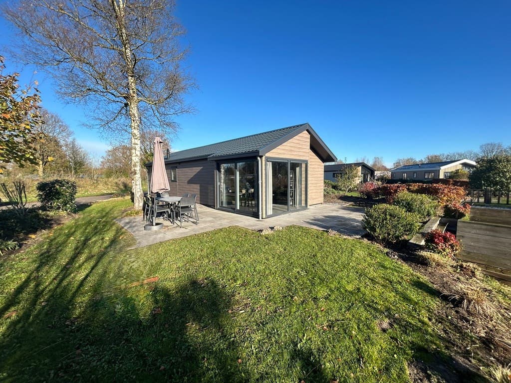 Moderne vakantiewoning met terras, liggend in een groene omgeving met bomen en struiken.