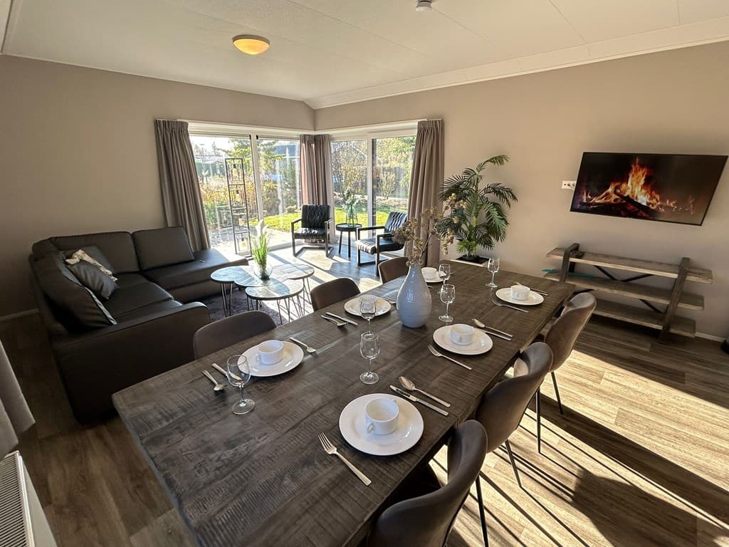 Woonkamer met eettafel, moderne meubels, grote ramen en uitzicht op de tuin