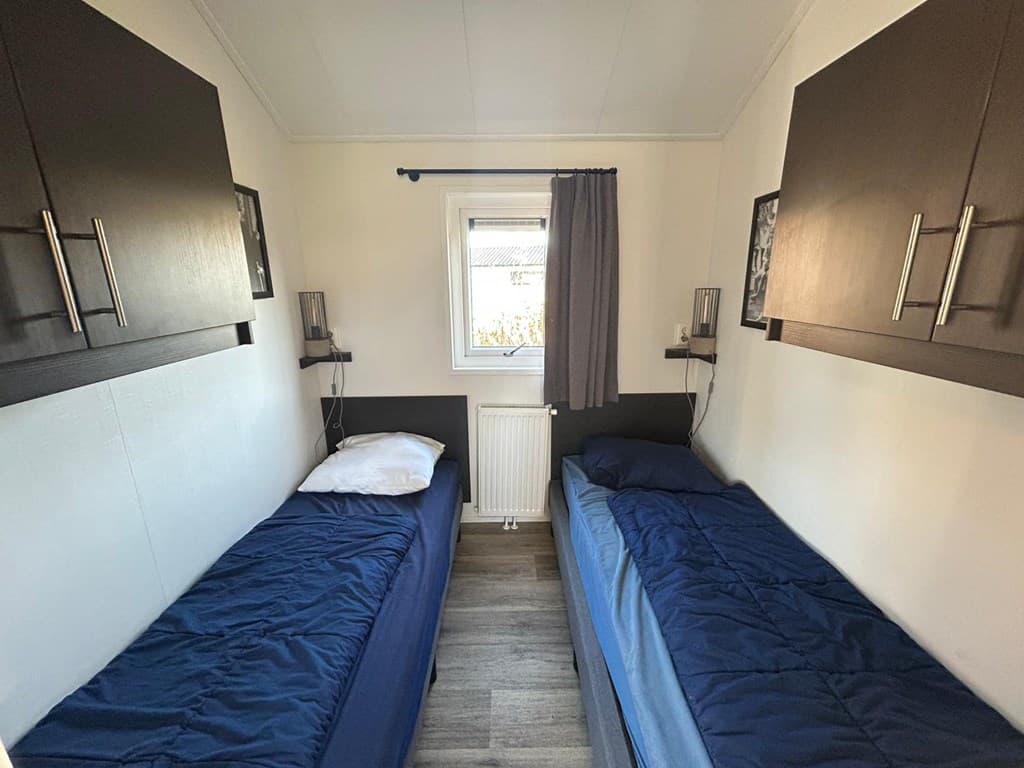 Slaapkamer met twee eenpersoonsbedden en wandkasten, voorzien van een raam met gordijn en een verwarming.