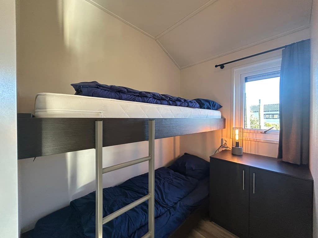 Slaapkamer met stapelbed en een kast, raam met uitzicht naar buiten en een lamp op de kast