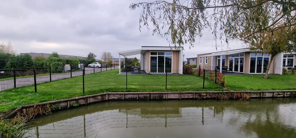 Tuin en vakantiewoning aan het water met een grasveld en een omheining rondom de locatie