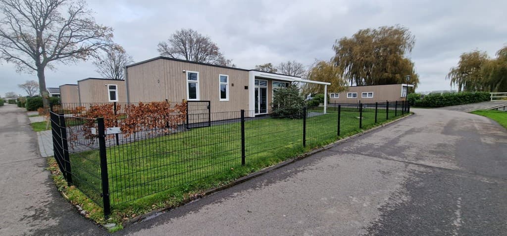 Moderne vakantiewoning met een verzorgd grasveld en omheining, gelegen aan een wandelpad en bomen in de omgeving