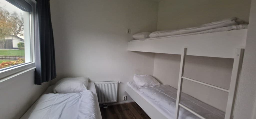 Slaapkamer met een eenpersoonsbed en een stapelbed, een raam met gordijnen en een radiator aan de muur.