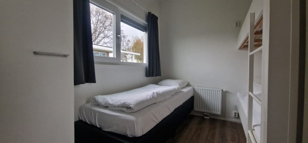 Slaapkamer met een eenpersoonsbed, gordijnen en kast, lichte muren en een radiator