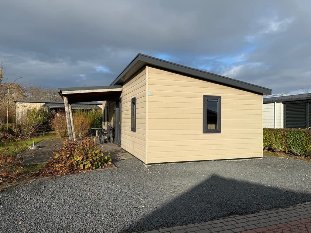 Lichte woning met een hellend dak, gelegen op een gravelperceel met een terras en groene beplanting.