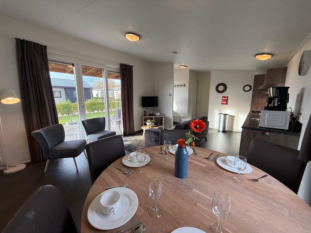 Eetruimte met houten tafel, stoelen, bank, televisie en toegang tot buitenruimte met een uitzicht op het groen