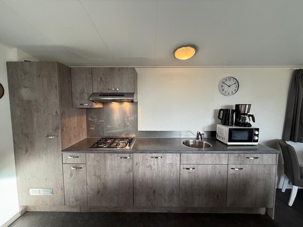 Keuken met grijze kasten, gasfornuis, spoelbak en enkele keukenapparaten, waaronder een koffiezetapparaat en magnetron.
